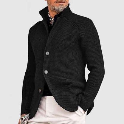 Giacca uomo elegante nera in maglia, con bottoni, indossata su camicia scura e pantaloni chiari. Stile casual chic, moda maschile autunnale.
