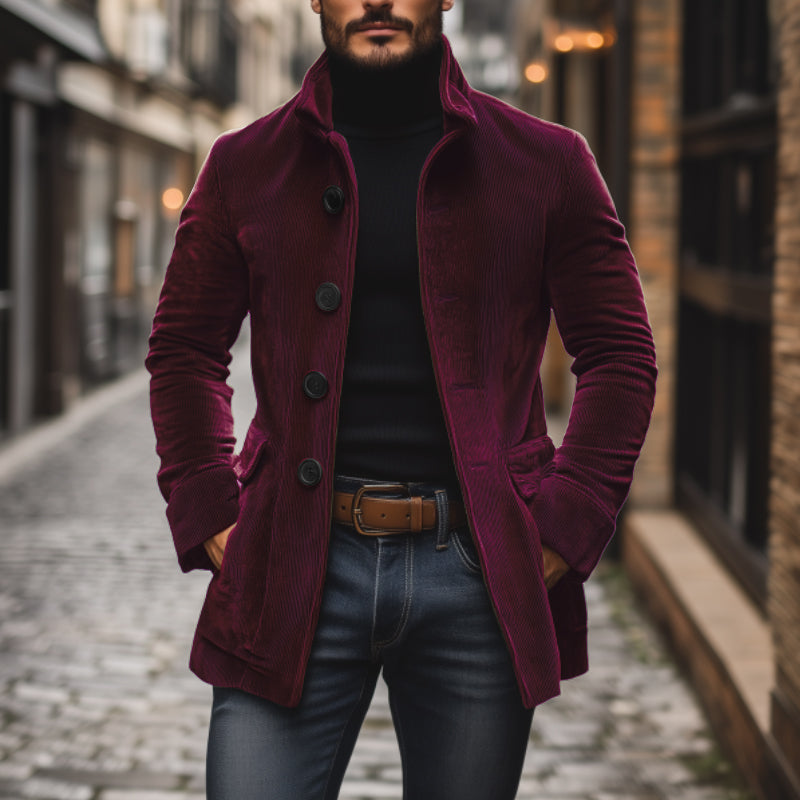Uomo con cappotto di velluto bordeaux, maglione nero e jeans, cammina su strada acciottolata. Moda autunnale, stile urbano elegante.