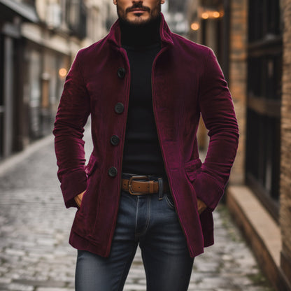 Uomo con cappotto di velluto bordeaux, maglione nero e jeans, cammina su strada acciottolata. Moda autunnale, stile urbano elegante.