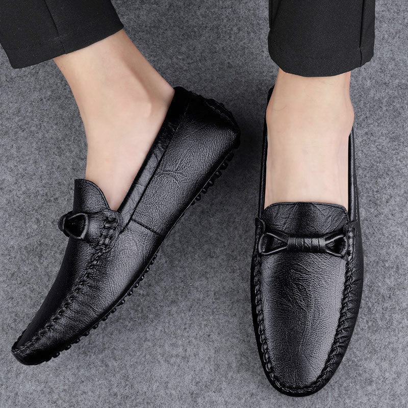 Scarpe mocassini uomo in pelle nera, eleganti e comode, su sfondo grigio. Design classico con fiocco decorativo, ideali per look formale.