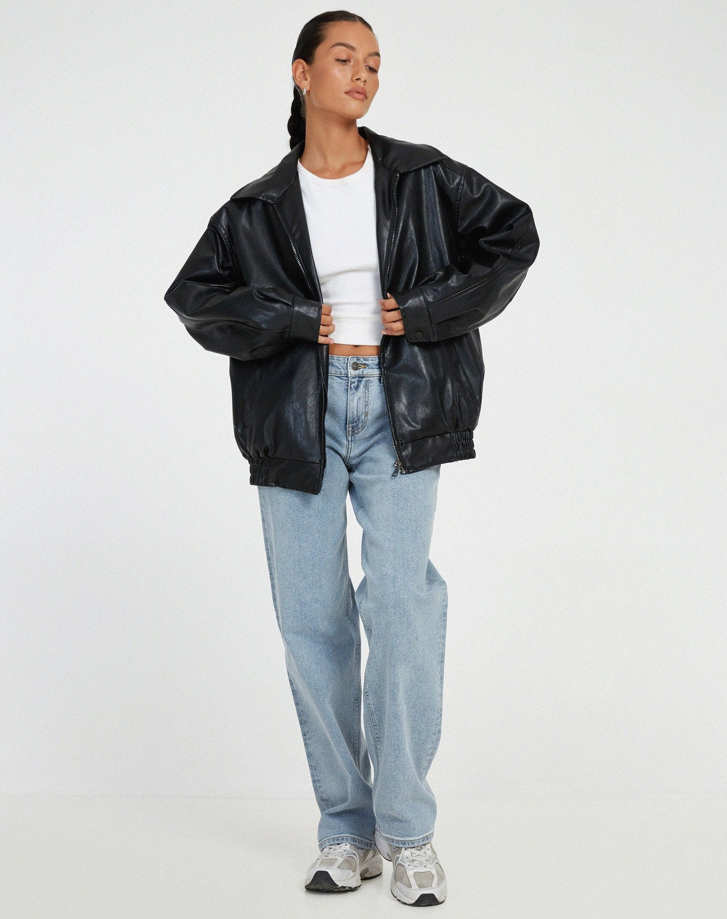 Donna con giacca di pelle nera, jeans larghi e sneakers bianche. Moda casual, stile urbano, abbigliamento autunnale. Sfondo bianco minimalista.