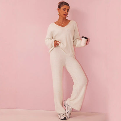 Donna in abbigliamento lounge bianco, con maglione e pantaloni larghi, tiene una tazza di caffè. Sfondo rosa, moda casual elegante.