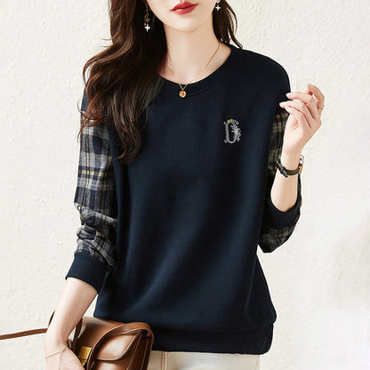 Donna con maglia blu scuro, maniche a quadri, indossa collana e orecchini. Borsa marrone a tracolla. Moda casual autunnale elegante.