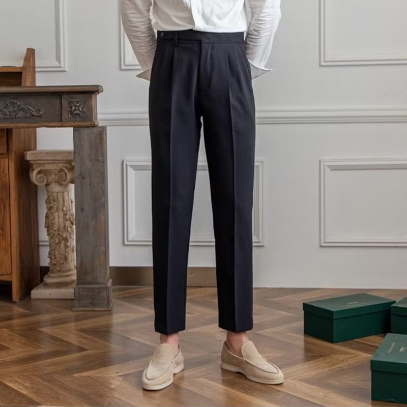 Pantaloni eleganti neri da uomo, abbinati a mocassini beige, su pavimento in legno. Moda maschile, abbigliamento formale, stile classico.
