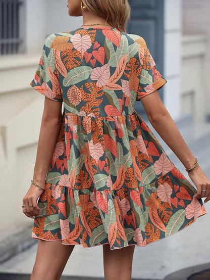 Donna con abito estivo a fantasia floreale colorata, sfondo urbano. Vestito corto, maniche corte, motivi foglie e fiori, moda femminile casual.