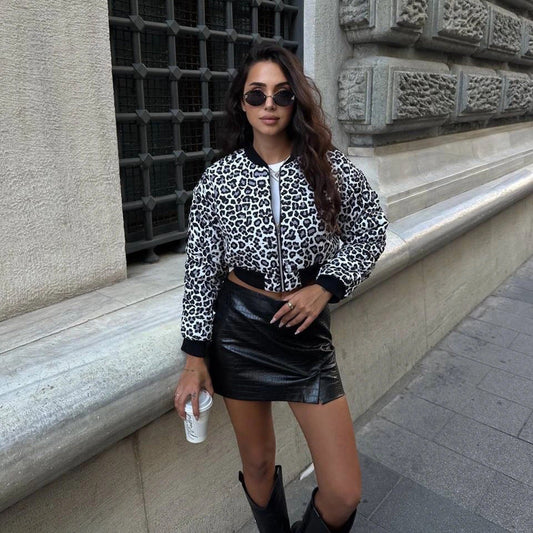 Donna con giacca leopardata e gonna in pelle nera, occhiali da sole, stivali neri, tiene un caffè. Moda urbana, stile autunnale, strada cittadina.