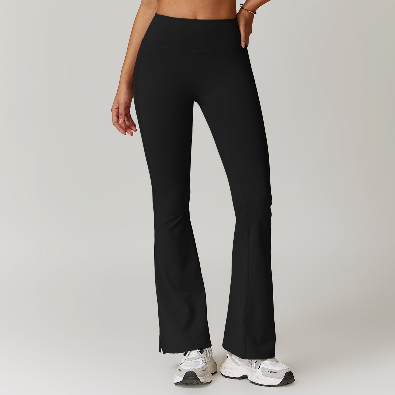 Pantaloni yoga neri a zampa, vita alta, indossati da una donna. Perfetti per fitness e moda casual. Scarpe da ginnastica bianche abbinate.