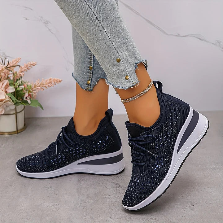 Scarpe da ginnastica nere con strass su pavimento grigio, indossate con jeans chiari. Eleganti e comode, ideali per moda casual e sportiva.