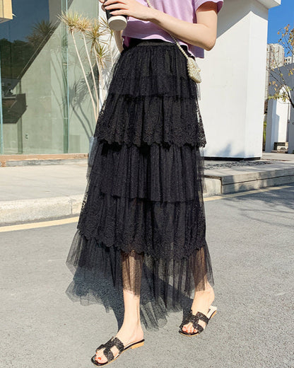 Donna con gonna lunga nera a balze in tulle, sandali eleganti, cammina su marciapiede urbano. Moda estiva, abbigliamento femminile chic.