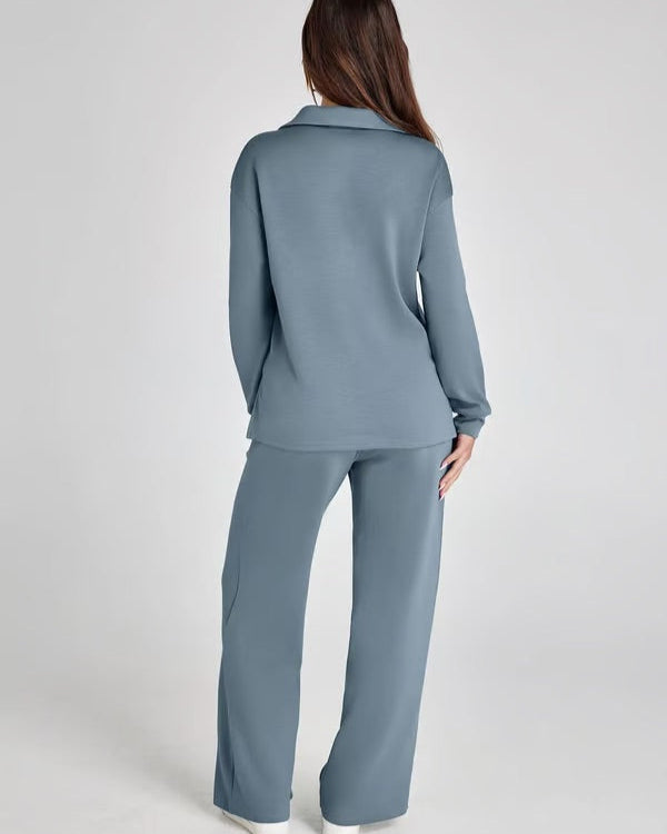 Donna di spalle indossa un completo loungewear blu grigio, composto da maglia a maniche lunghe e pantaloni larghi. Stile casual e confortevole.