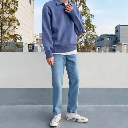Uomo in maglione blu e jeans chiari su terrazza urbana, indossa scarpe da ginnastica bianche. Moda casual maschile, abbigliamento autunnale.