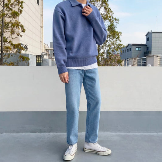 Uomo in maglione blu e jeans chiari su terrazza urbana, indossa scarpe da ginnastica bianche. Moda casual maschile, abbigliamento autunnale.