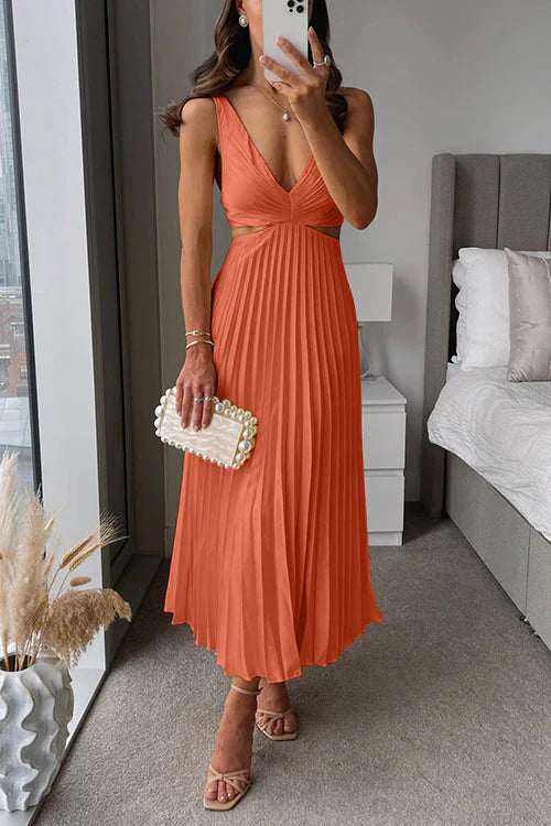 Donna in abito lungo arancione plissettato con scollo a V, borsa bianca con perle, sandali beige. Interno moderno con letto e finestra panoramica.