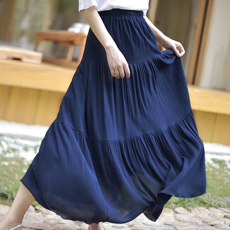 Donna con gonna lunga blu plissettata, camminando su un sentiero di pietra. Moda estiva, abbigliamento casual elegante, tendenza femminile.