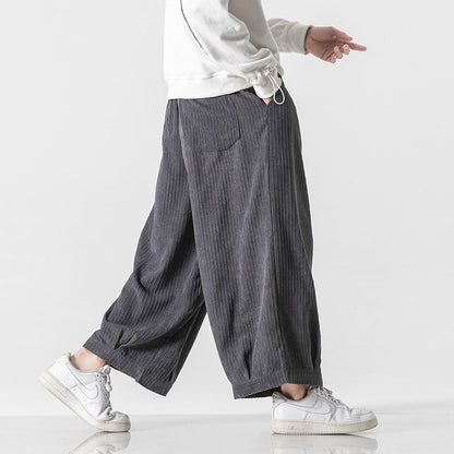 Pantaloni larghi grigi a righe, indossati con felpa bianca e sneakers bianche. Moda casual uomo, stile urbano, comfort quotidiano.