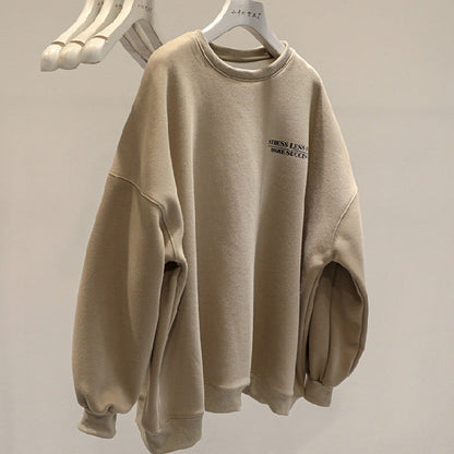 Felpa beige oversize con scritta "STRESS LESS MAKE SUCCESS", appesa su gruccia bianca. Moda casual, abbigliamento comodo, tendenze streetwear.