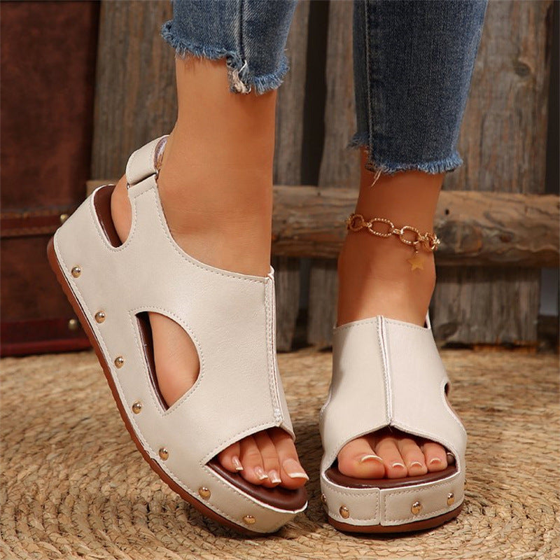 Sandali bianchi in pelle con borchie dorate, indossati con jeans strappati. Design aperto, comodi e alla moda per l'estate.