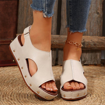Sandali bianchi in pelle con borchie dorate, indossati con jeans strappati. Design aperto, comodi e alla moda per l'estate.