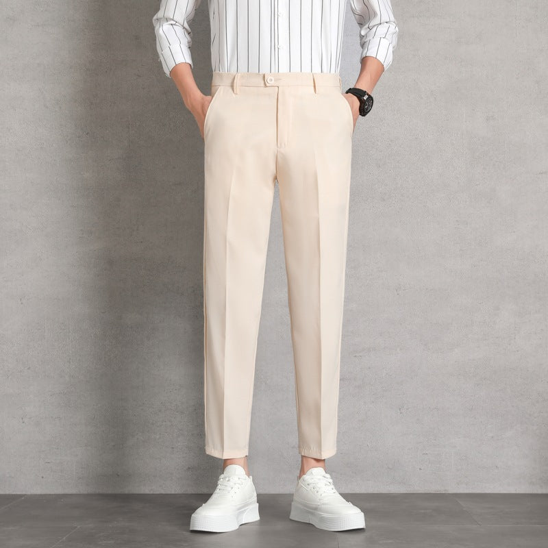Uomo in pantaloni beige eleganti, camicia a righe bianche, scarpe da ginnastica bianche, posa casual su sfondo grigio. Moda maschile contemporanea.