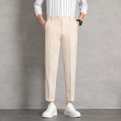 Uomo in pantaloni beige eleganti, camicia a righe bianche, scarpe da ginnastica bianche, posa casual su sfondo grigio. Moda maschile contemporanea.