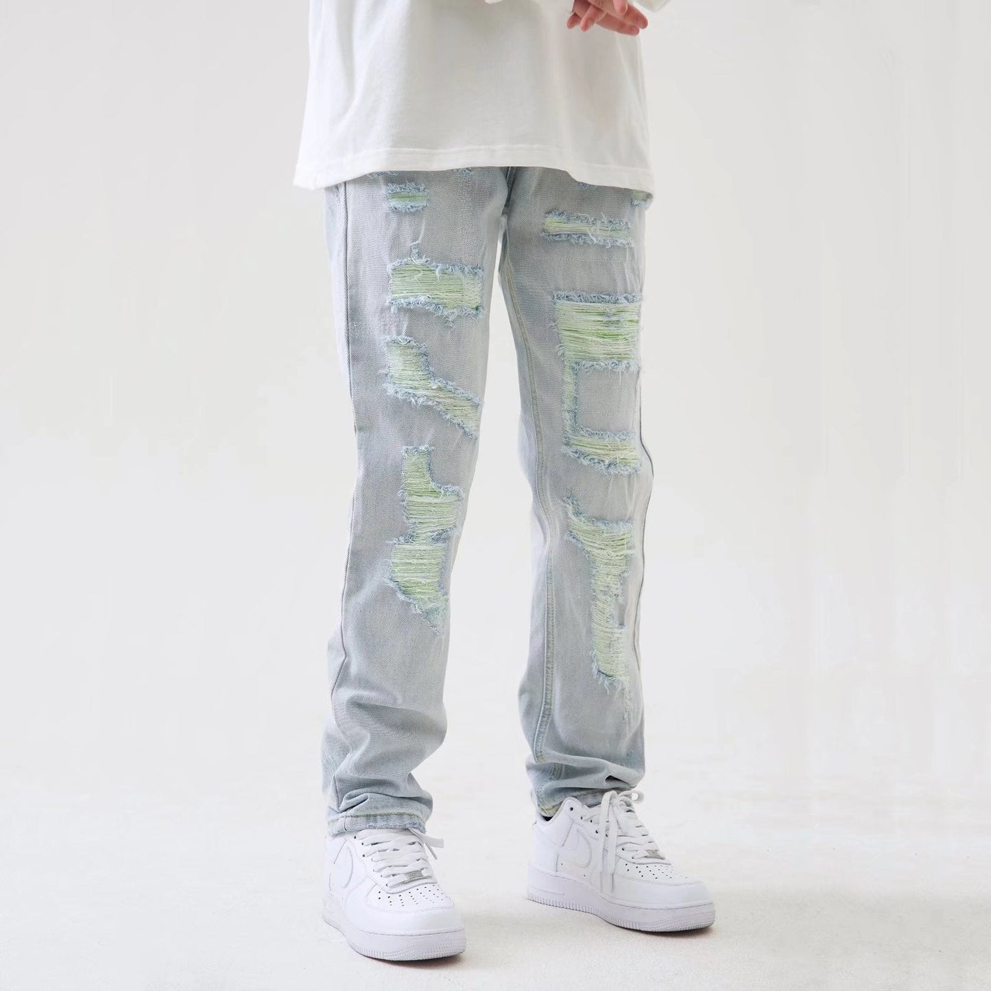 Jeans strappati chiari con dettagli verdi, indossati con scarpe da ginnastica bianche e maglietta bianca. Moda casual uomo, stile urbano.