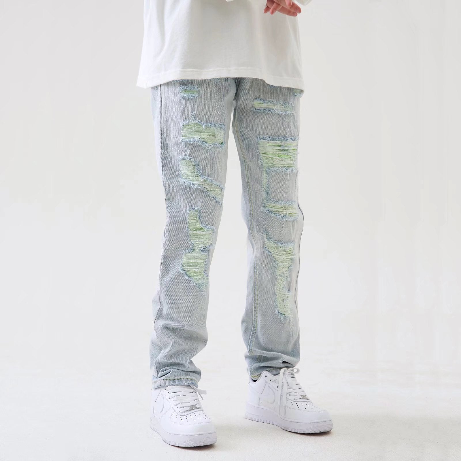 Jeans strappati chiari con dettagli verdi, indossati con scarpe da ginnastica bianche e maglietta bianca. Moda casual uomo, stile urbano.