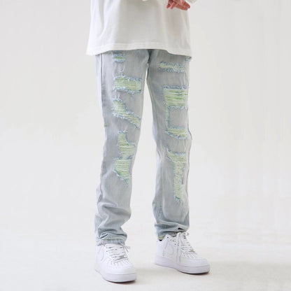 Jeans strappati chiari con dettagli verdi, indossati con scarpe da ginnastica bianche e maglietta bianca. Moda casual uomo, stile urbano.