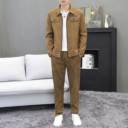 Uomo in abito casual marrone, giacca e pantaloni coordinati, su tappeto grigio. Sfondo con divano bianco e decorazioni moderne.