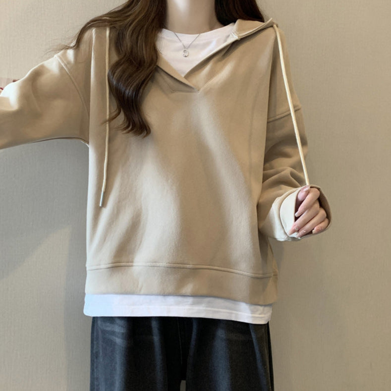 Donna con felpa beige oversize, cappuccio e lacci, indossa maglietta bianca e pantaloni neri. Moda casual autunnale, abbigliamento comodo.