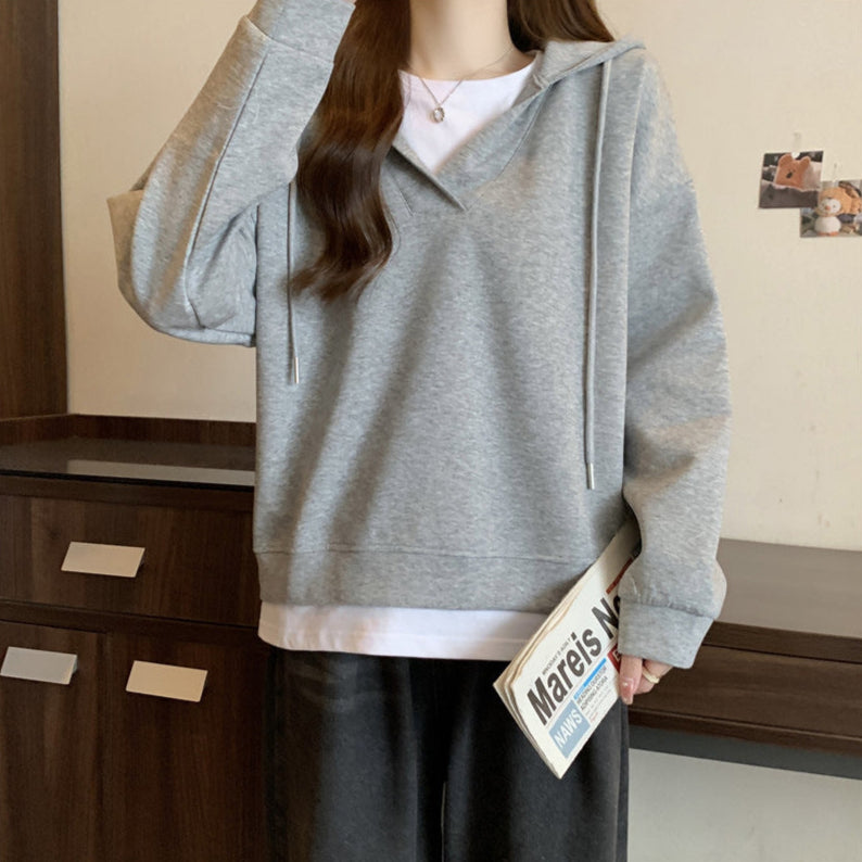 Donna con felpa grigia casual, cappuccio e lacci, tiene una rivista. Look moderno e confortevole, ideale per moda autunnale e streetwear.