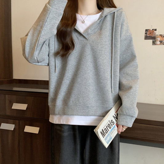 Donna con felpa grigia casual, cappuccio e lacci, tiene una rivista. Look moderno e confortevole, ideale per moda autunnale e streetwear.