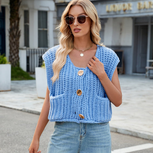 Donna con occhiali da sole indossa un gilet blu lavorato a maglia con bottoni grandi, in posa all'aperto. Moda casual, abbigliamento estivo, stile urbano.