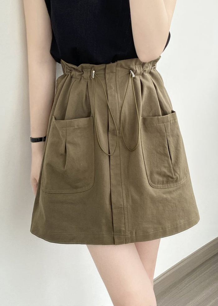 Gonna corta verde oliva con tasche frontali e coulisse, indossata con top nero. Moda casual femminile, abbigliamento estivo trendy.