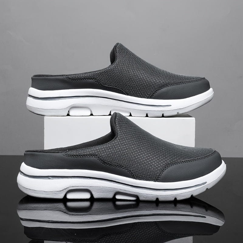 Scarpe slip-on nere da uomo su sfondo grigio, design sportivo con suola bianca ammortizzata, tessuto traspirante, moda casual e comfort.