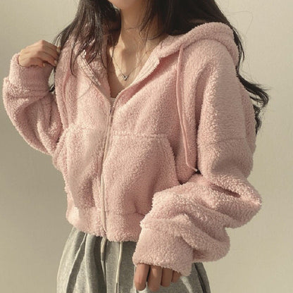 Donna con felpa rosa in pile, cappuccio e zip, indossa pantaloni grigi. Moda casual autunnale, abbigliamento comodo e caldo.