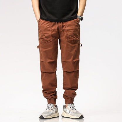 Pantaloni cargo marroni da uomo, tasche multiple, stile casual, abbinati a scarpe sportive bianche e nere, moda maschile contemporanea.