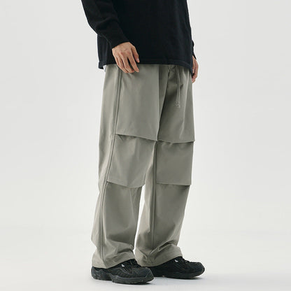 Pantaloni cargo grigi da uomo, design ampio e moderno, con tasche multiple. Indossati con maglia nera e scarpe sportive nere. Moda casual maschile.