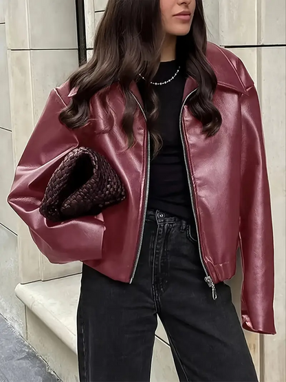 Donna con giacca di pelle rossa, maglia nera e jeans scuri, tiene una borsa intrecciata marrone. Moda autunnale urbana elegante.