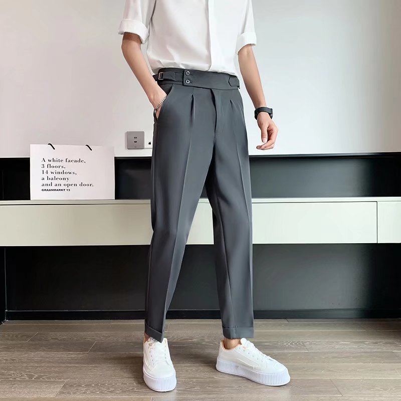 Uomo in pantaloni grigi eleganti con cintura alta, camicia bianca e sneakers bianche. Moda maschile moderna, abbigliamento casual chic.