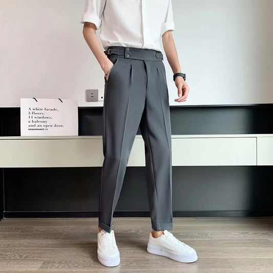 Uomo in pantaloni grigi eleganti con cintura alta, camicia bianca e sneakers bianche. Moda maschile moderna, abbigliamento casual chic.