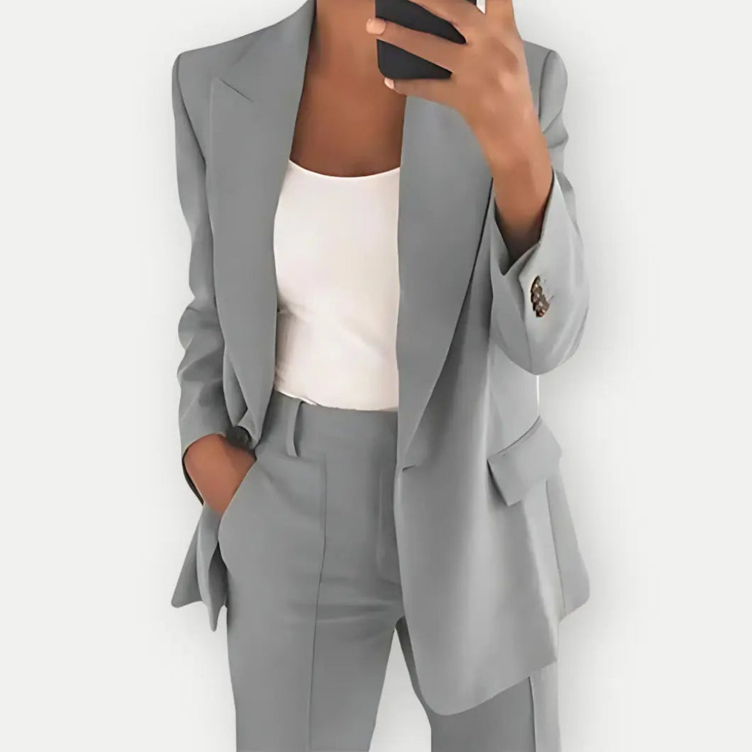 Completo donna elegante grigio, giacca e pantaloni abbinati, indossato con top bianco. Moda business casual, abbigliamento formale femminile.