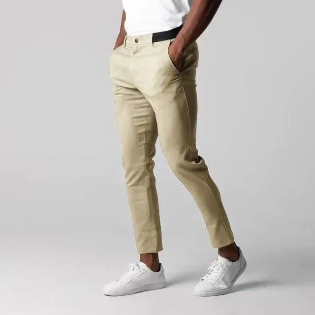 Pantaloni chino beige da uomo, eleganti e casual, abbinati a scarpe da ginnastica bianche e maglietta bianca, moda maschile moderna.