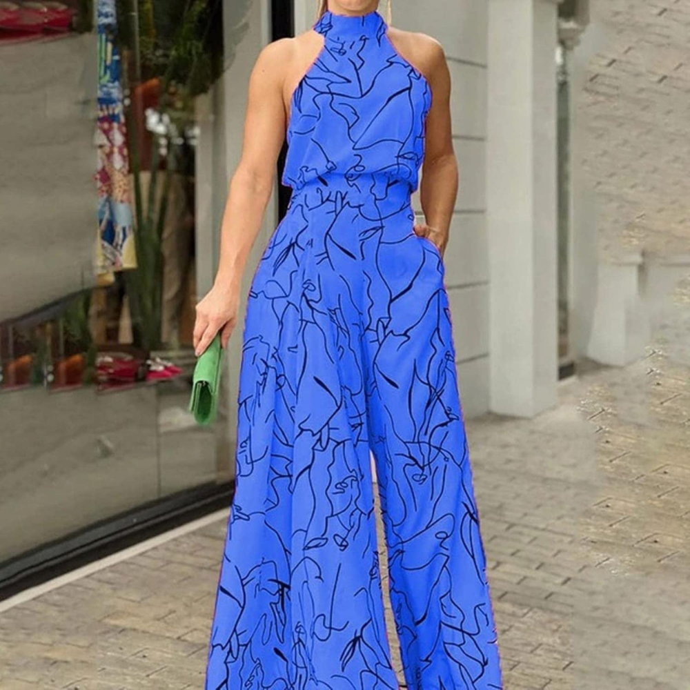 Donna in tuta blu con motivo astratto nero, borsa verde, davanti a una vetrina. Moda estiva elegante, abbigliamento casual chic.