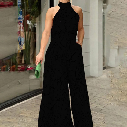 Donna in elegante tuta nera senza maniche, con borsa verde, cammina su marciapiede urbano. Moda femminile, abbigliamento estivo, stile chic.
