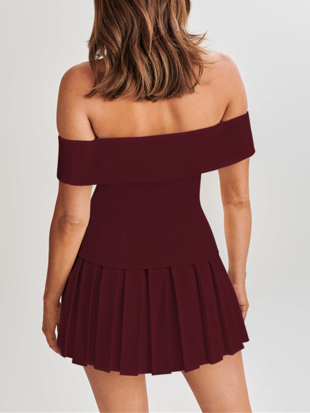 Donna in abito bordeaux senza spalline, design a pieghe, sfondo neutro. Moda elegante, abbigliamento femminile, stile serale.