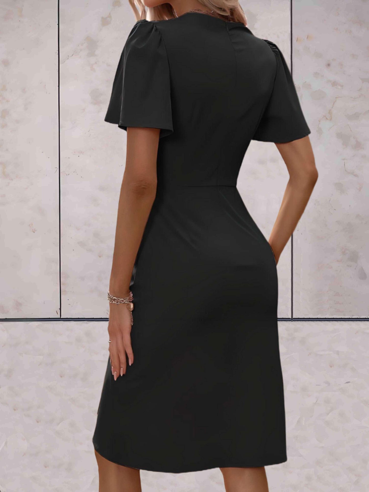 Abito nero elegante da donna, maniche corte, lunghezza al ginocchio, indossato da una modella di spalle, sfondo marmo chiaro.