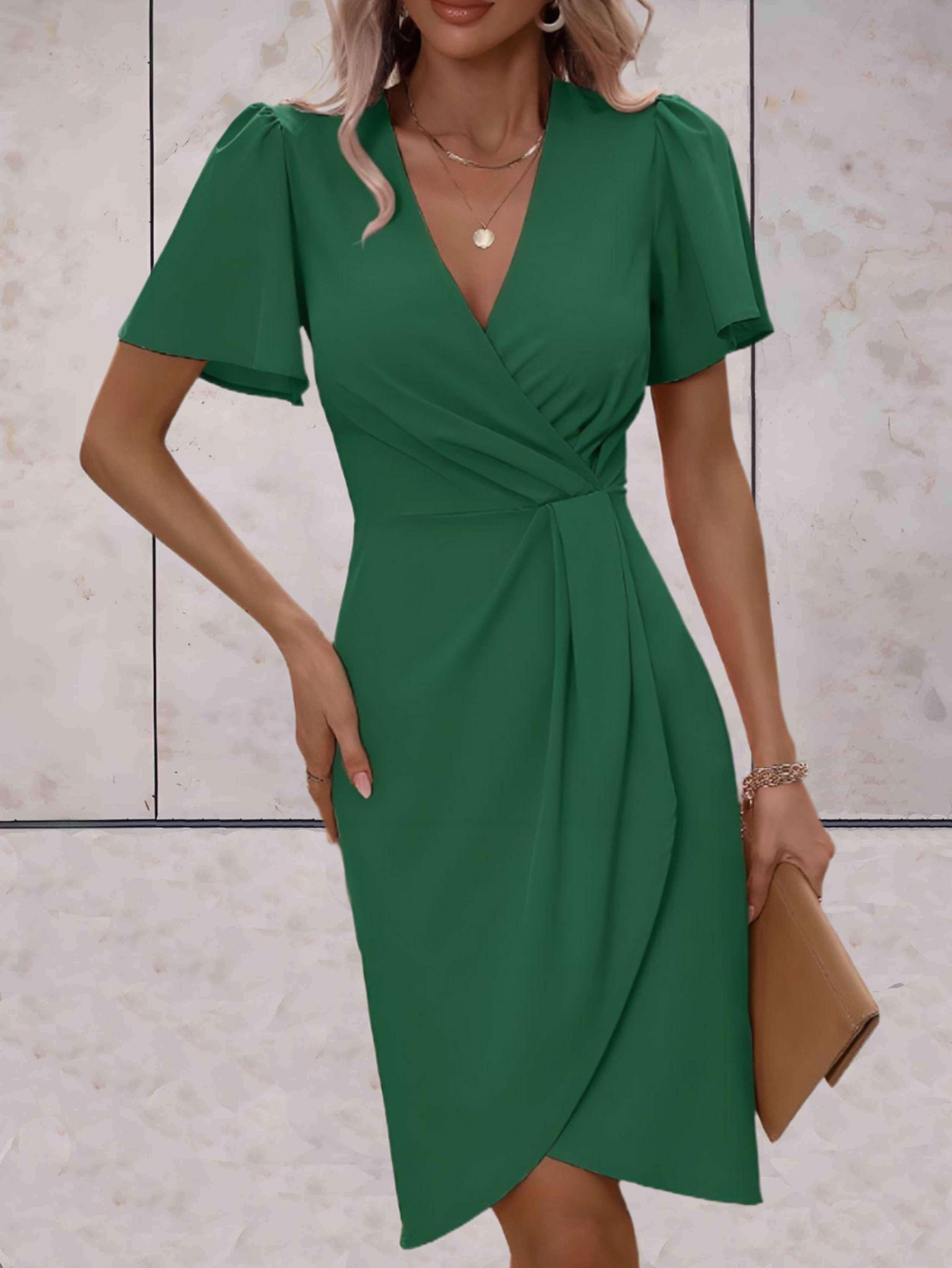 Abito verde elegante con scollo a V e maniche corte, indossato da una donna. Accessori: collana, bracciale e pochette beige. Moda femminile chic.