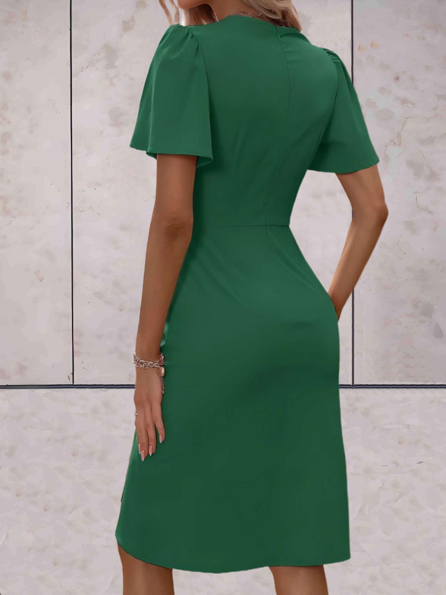 Abito verde elegante da donna, maniche corte, lunghezza al ginocchio, sfondo marmo chiaro. Moda femminile, abbigliamento chic, stile sofisticato.