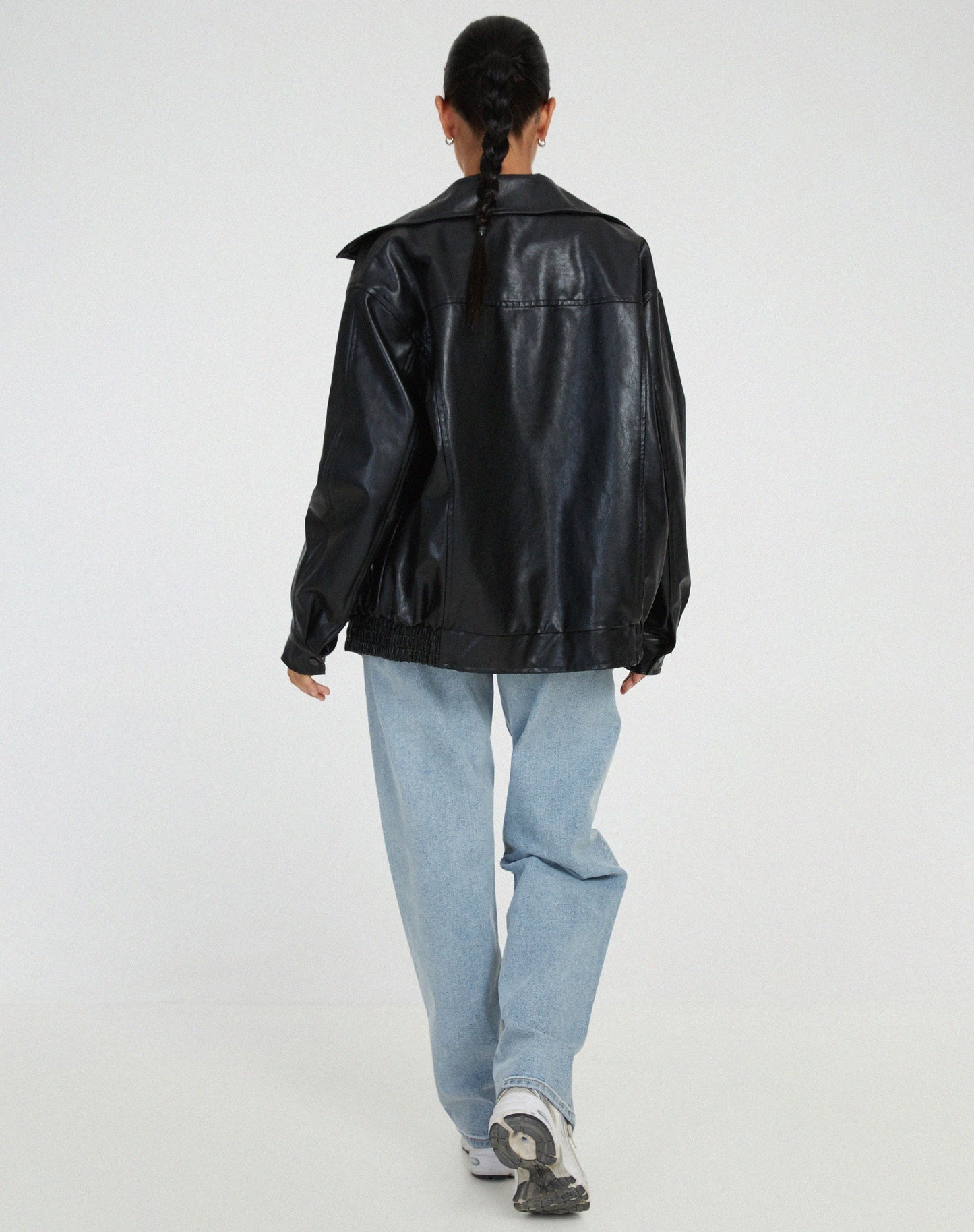 Donna di spalle con giacca di pelle nera, jeans larghi e scarpe da ginnastica bianche. Moda casual, stile urbano, abbigliamento autunnale.