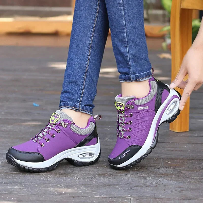 Scarpe da ginnastica viola da donna con suola ammortizzata, indossate con jeans. Design sportivo, comfort e stile casual per passeggiate all'aperto.